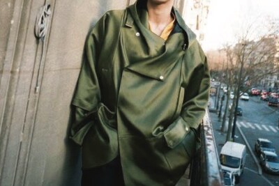 Editorial placeholder image: an olive overcoat against a sunlit facade above a city street.