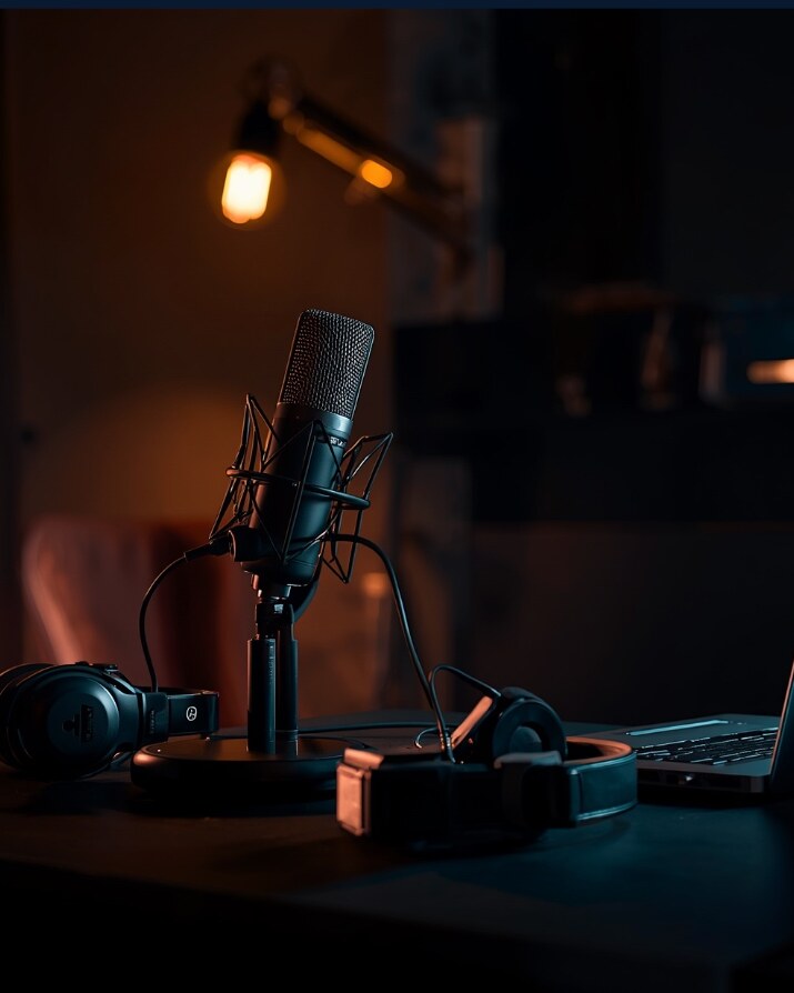 Podcast microphone, headphones and laptop in a warmly lit studio.